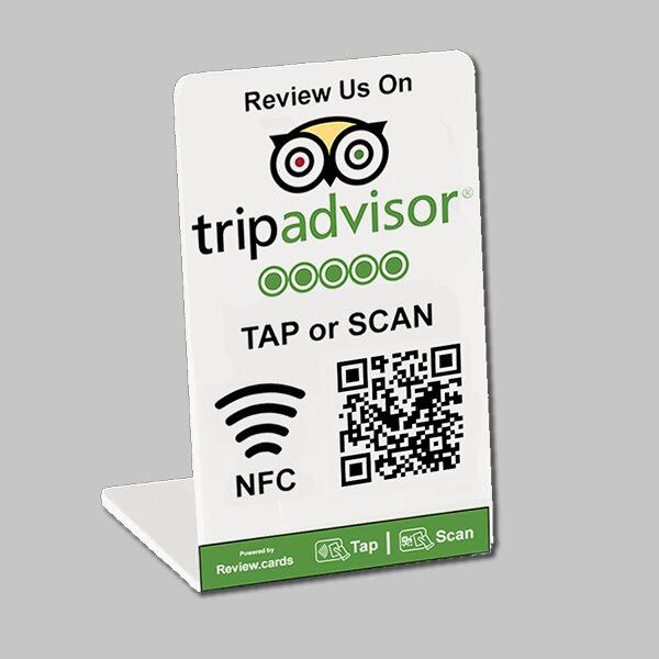 A small, white, L-shaped display card featuring the TripAdvisor logo and the text "Review Us On tripadvisor". Below are five green circles, the words "TAP or SCAN NFC", a QR code, and icons for NFC and QR scanning. The base has icons and the text "Powered by Review.cards".