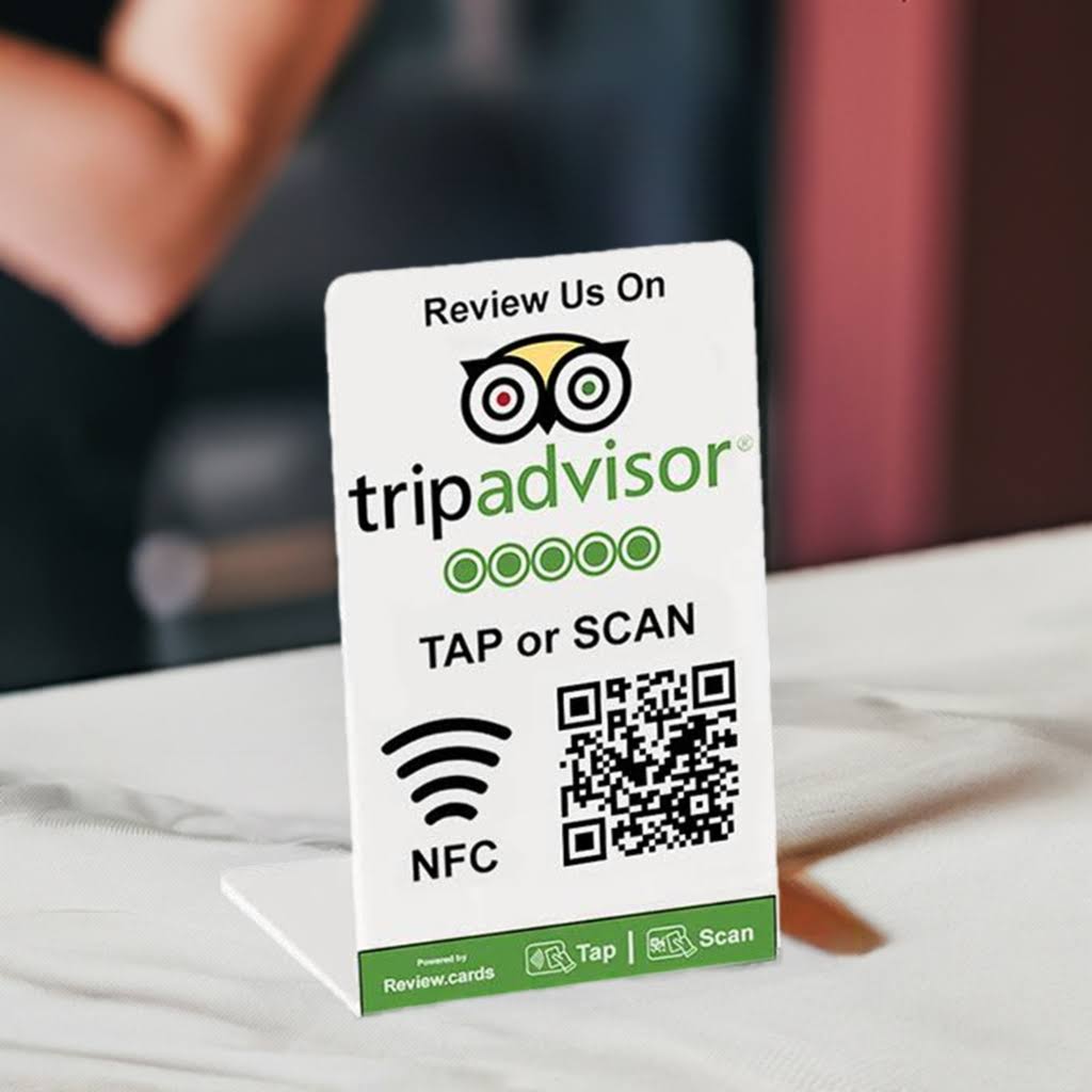 A small standing sign on the table encourages patrons to review the establishment on TripAdvisor. The Hospitality Bundle 1 table tent features the TripAdvisor logo, "TAP or SCAN" instructions, an NFC symbol, and a QR code. The sign is supported by a white base.